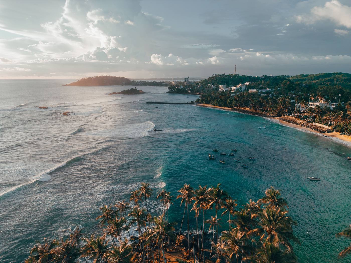 Aerial view of a turquoise bay lined with palm trees and fishing boats on Sri Lanka's south coast
